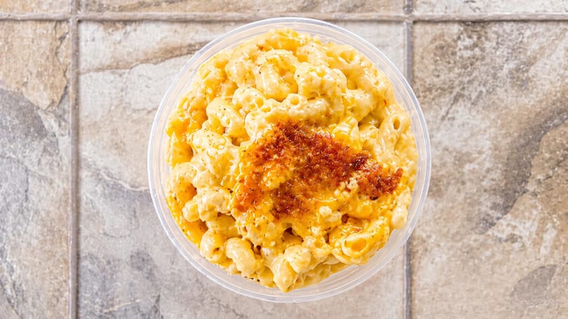 Overhead view of a clear plastic container filled with creamy macaroni and cheese, topped with seasoning.