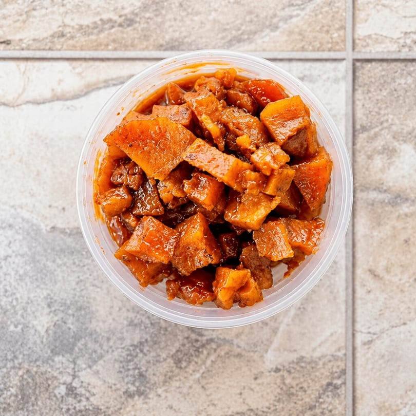 Overhead view of a clear plastic container filled with diced, saucy sweet potatoes.